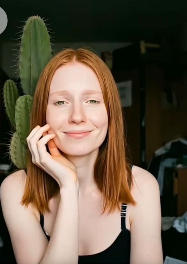O da ruiva aparece olhando para vocên com um meio sorriso nos lábioas srgurando o queixo com uma das mâos.rosto